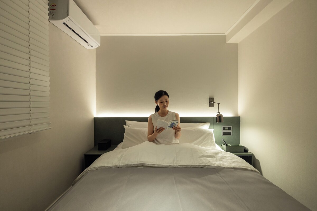 Habitación de hotel con cama, mesita de noche, aire acondicionado y lámpara de pared.