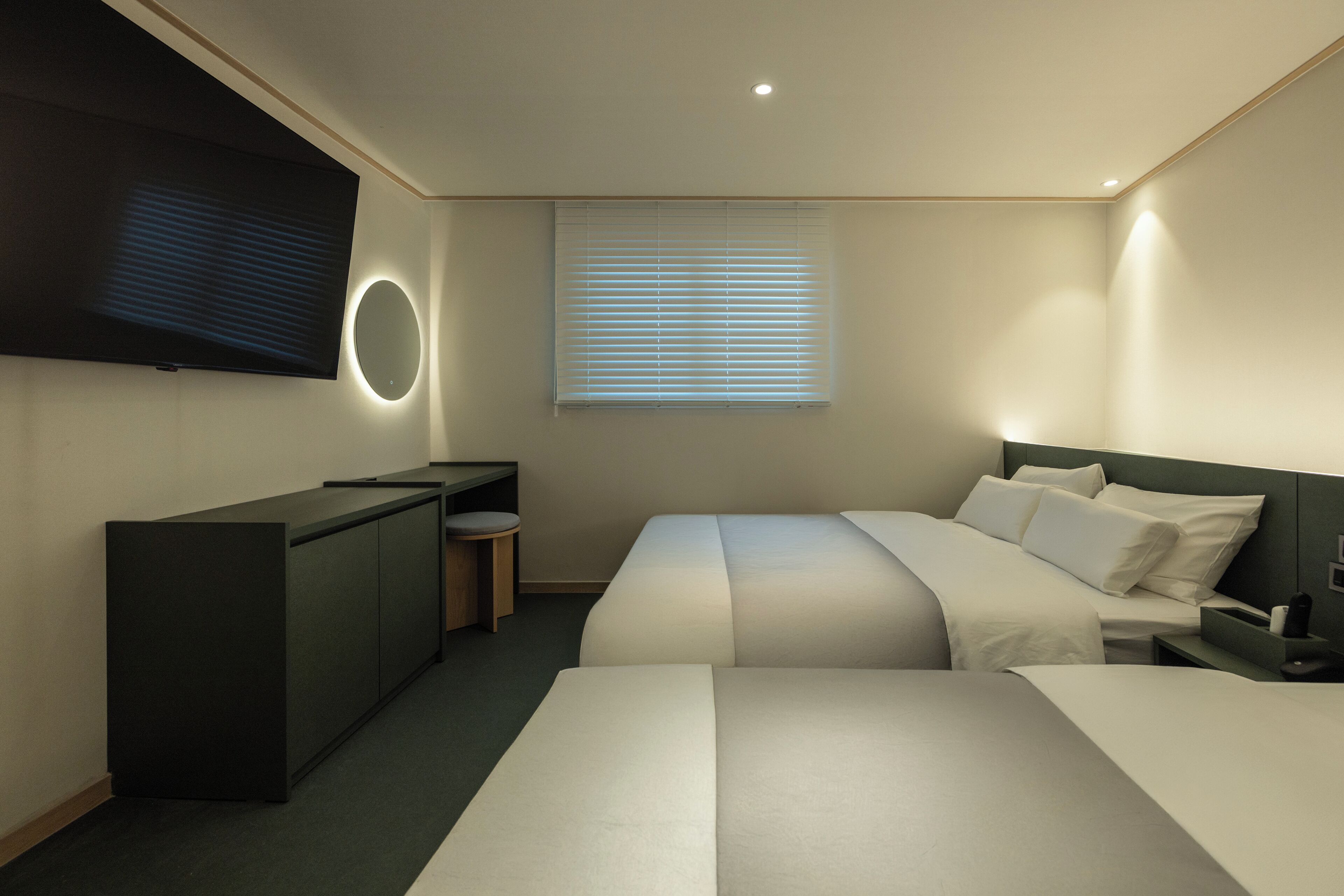 Una habitación de hotel moderna con una televisión de pantalla plana, una cama, una mesita de noche, un escritorio con una silla y una ventana con persianas.