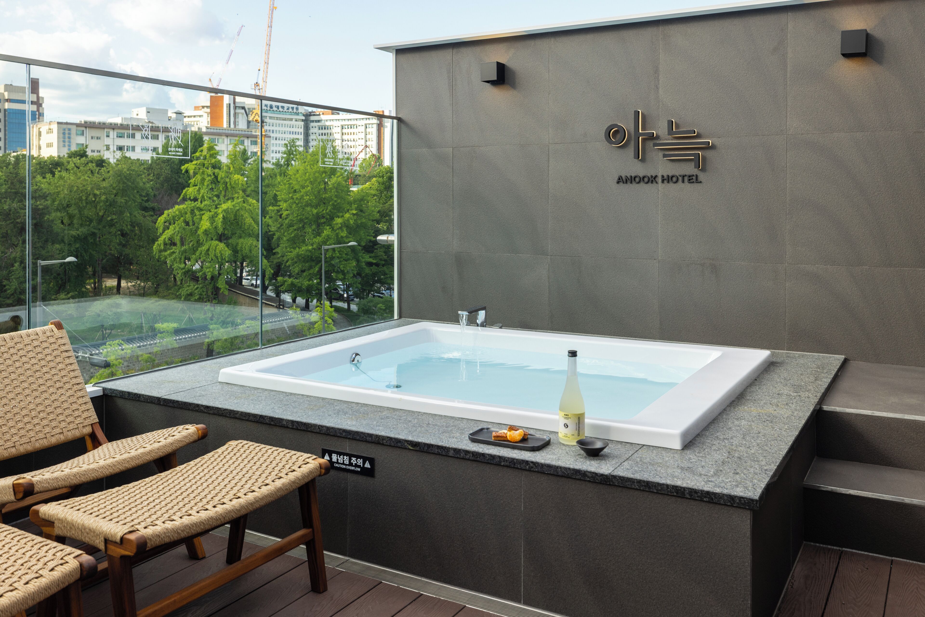 Una habitación de hotel moderna con una bañera grande, sillas de mimbre y vista a la ciudad.