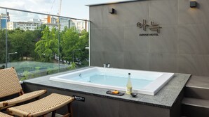 A modern hotel room with a large bathtub, wicker chairs, and a view of the cityscape.