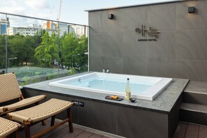 A modern hotel room with a large bathtub, wicker chairs, and a view of the cityscape.