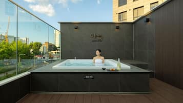 A person in a hot tub with a city view, a caution sign, and a bottle on the side.