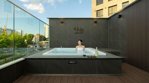 Una persona en un jacuzzi con vista a la ciudad, un letrero de precaución y una botella a un lado.
