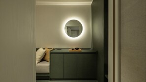 A small, dimly lit room with a single bed, a bedside table, and a mirror with a circular light.
