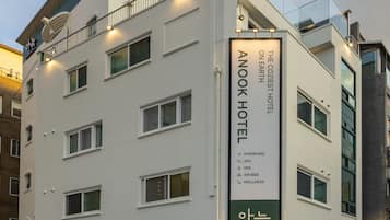 Un moderno edificio de hotel con un cartel llamativo del Hotel Anook, que ofrece servicios como habitaciones estándar, 2PC, SPA, Air B&B y servicios de bienestar.