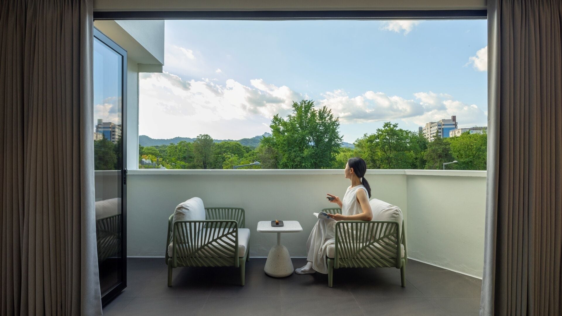A balcony with two wicker chairs, a small table, and a person using a mobile device.