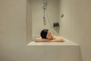 Una persona descansando en una bañera con un cabezal de ducha encima.