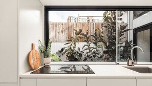 A modern kitchen with a black countertop, a wooden cutting board, a potted plant, and a view of a wooden fence and buildings outside. - Modern Designer Terrace Next to Surry Hills (Redfern)