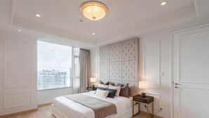 Een slaapkamer met een groot bed, een gestapeld hoofdeinde, nachtkastjes met lampen, uitzicht door een raam en een deur.