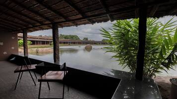 Un espacio al aire libre con sillas y una mesa, con vista a un cuerpo de agua y vegetación.