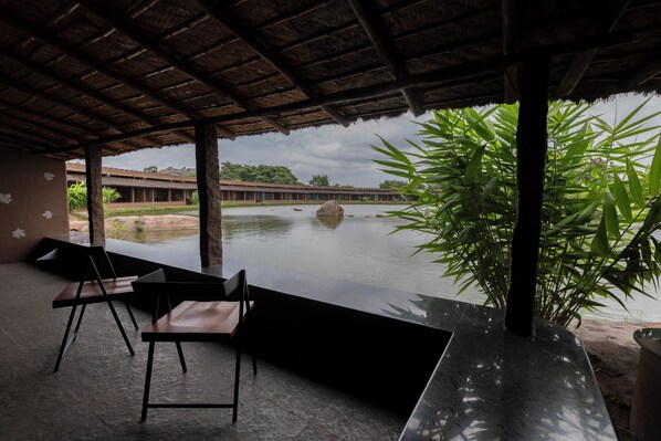 Un espacio al aire libre con sillas y una mesa, con vista a un cuerpo de agua y vegetación.