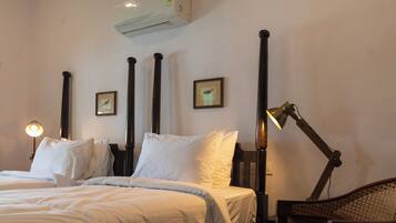 A hotel room with a bed, a desk, a chair, a desk lamp, and an air conditioner.