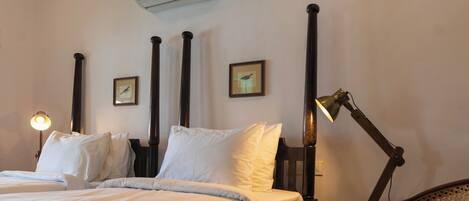 Quarto de hotel com cama, escrivaninha, cadeira, luminária de mesa e ar condicionado.