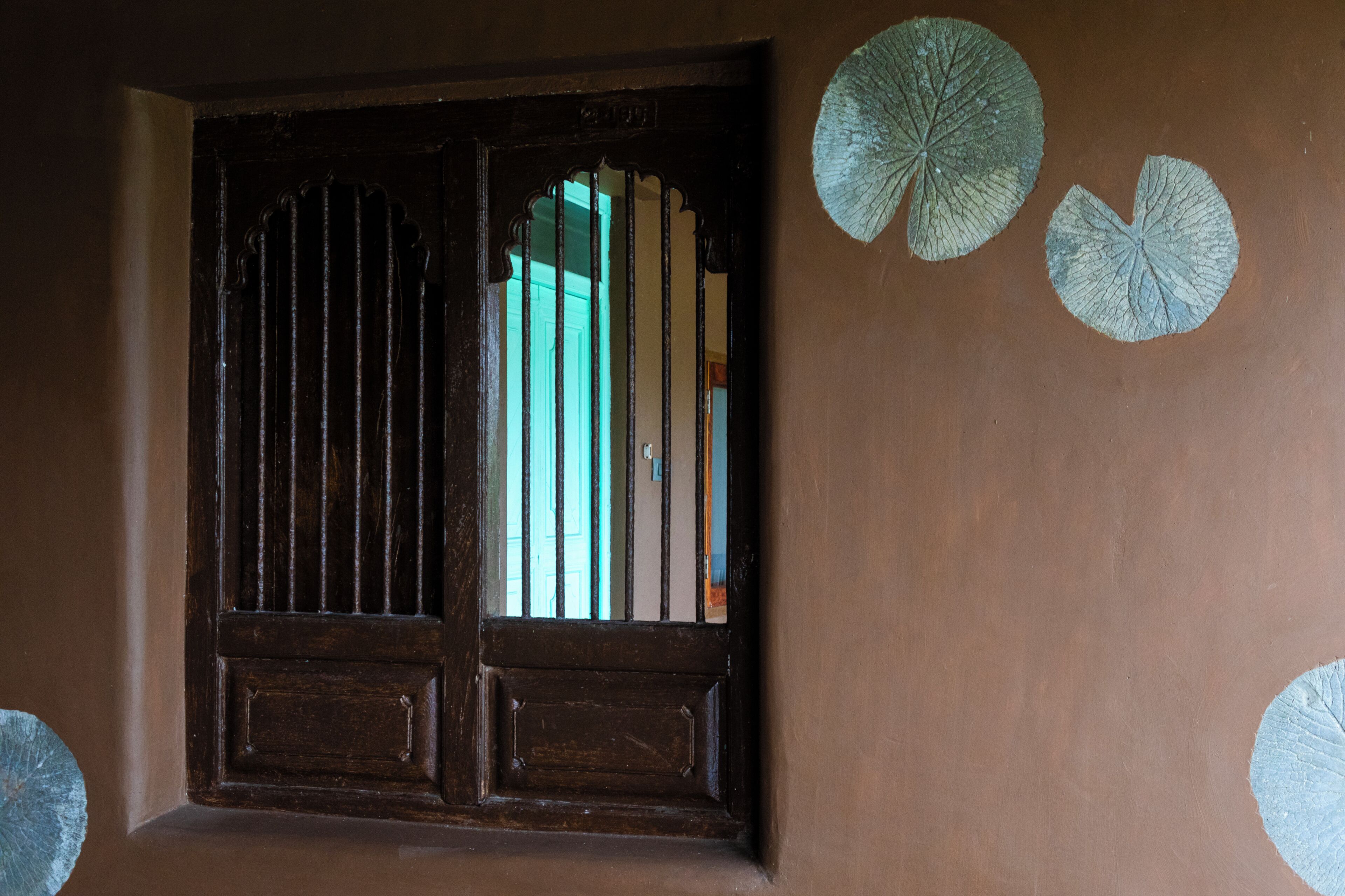 Una puerta de madera con barrotes verticales, una ventana con vistas y dos adornos circulares en la pared.