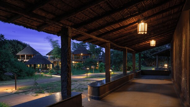 A covered outdoor area with a thatched-roof structure, stone benches, and ambient lighting. - Hampi's Feathers Resort (Koppal)