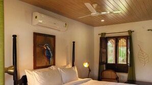 A bedroom with a bed, a ceiling fan, an air conditioning unit, a window with curtains, and a wall-mounted lamp. - Hampi's Feathers Resort (Koppal)