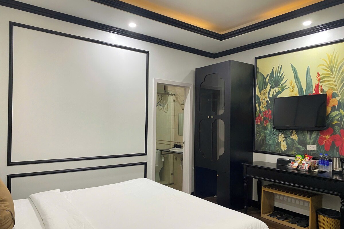 A hotel room with a bed, a wardrobe, a television, and a wall with a floral mural.