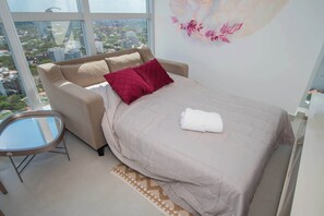 Ein Schlafzimmer mit Bett, Sofa, Glastisch und Blick auf die Stadt.