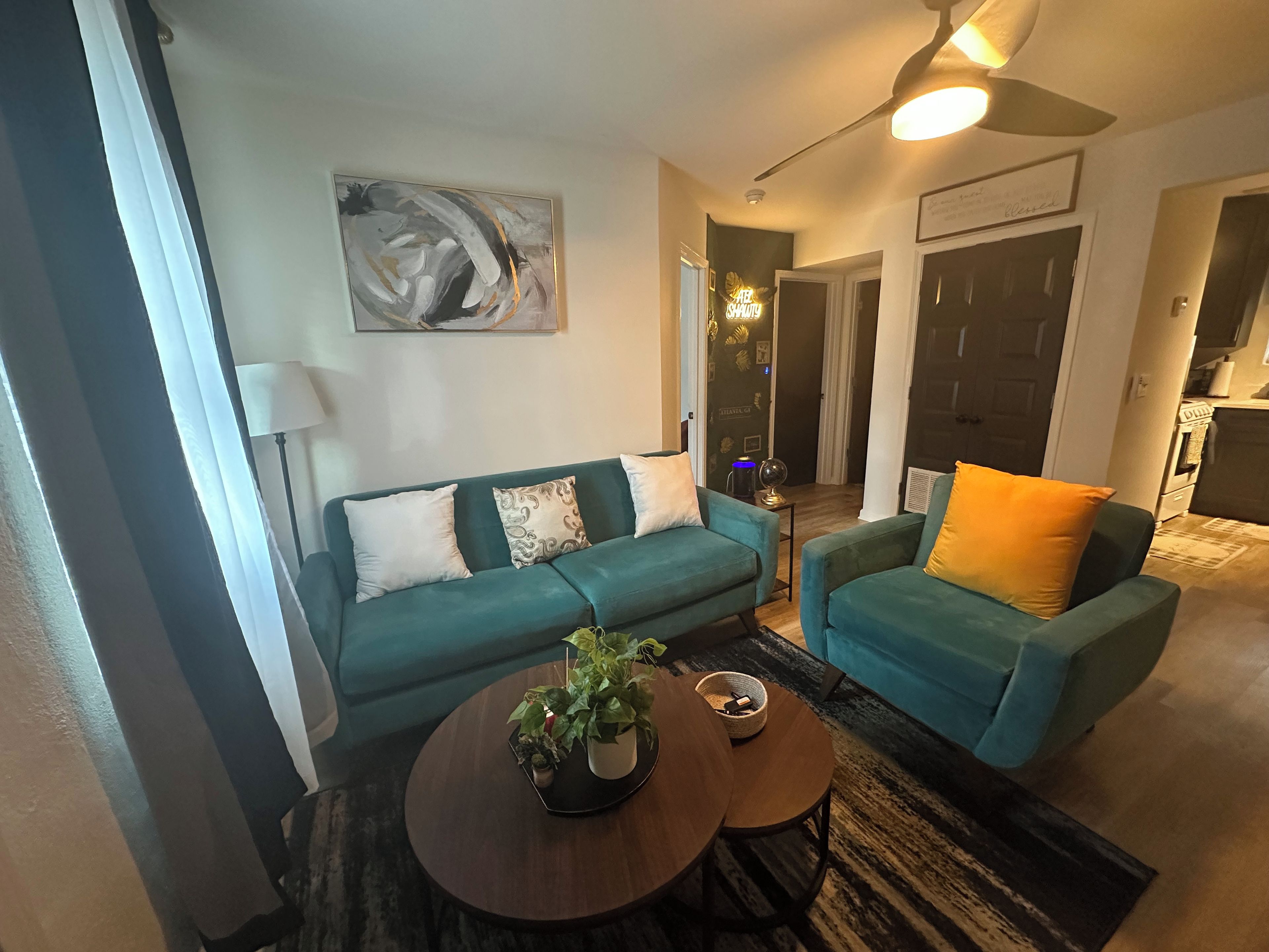 A living room with teal sofas, a coffee table, a painting, and a ceiling fan.