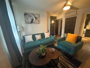 A living room with teal sofas, a coffee table, a painting, and a ceiling fan. - Summerhill Stays  Walk to GSU Stadium  Sleeps 7 (Atlanta)