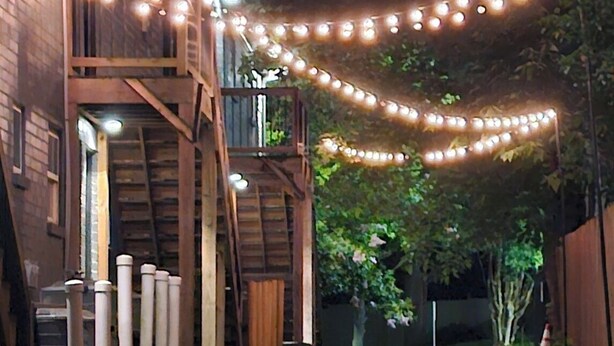 A wooden building with a balcony, string lights, and a wet ground. - Stay in the Heart of Atlanta Comfortable, Stylish & Close to Everything (Atlanta)