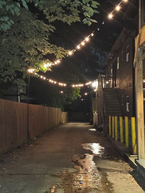 A narrow alleyway with string lights overhead, a wooden fence on one side, and a building with a wooden exterior on the other. - Summerhill Stays  Walk to GSU Stadium  Sleeps 7 (Atlanta)