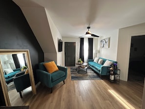Un salon moderne avec un canapé de couleur turquoise, un fauteuil assorti, une table basse et un ventilateur de plafond.
