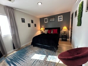 Un dormitorio con una cama, dos lámparas de noche, una silla roja, un tapete estampado y cuadros en la pared.