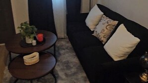 A living room with a black sofa, a small round table with a plant, a lamp, and a painting on the wall. - Stay in the Heart of Atlanta Comfortable, Stylish & Close to Everything (Atlanta)