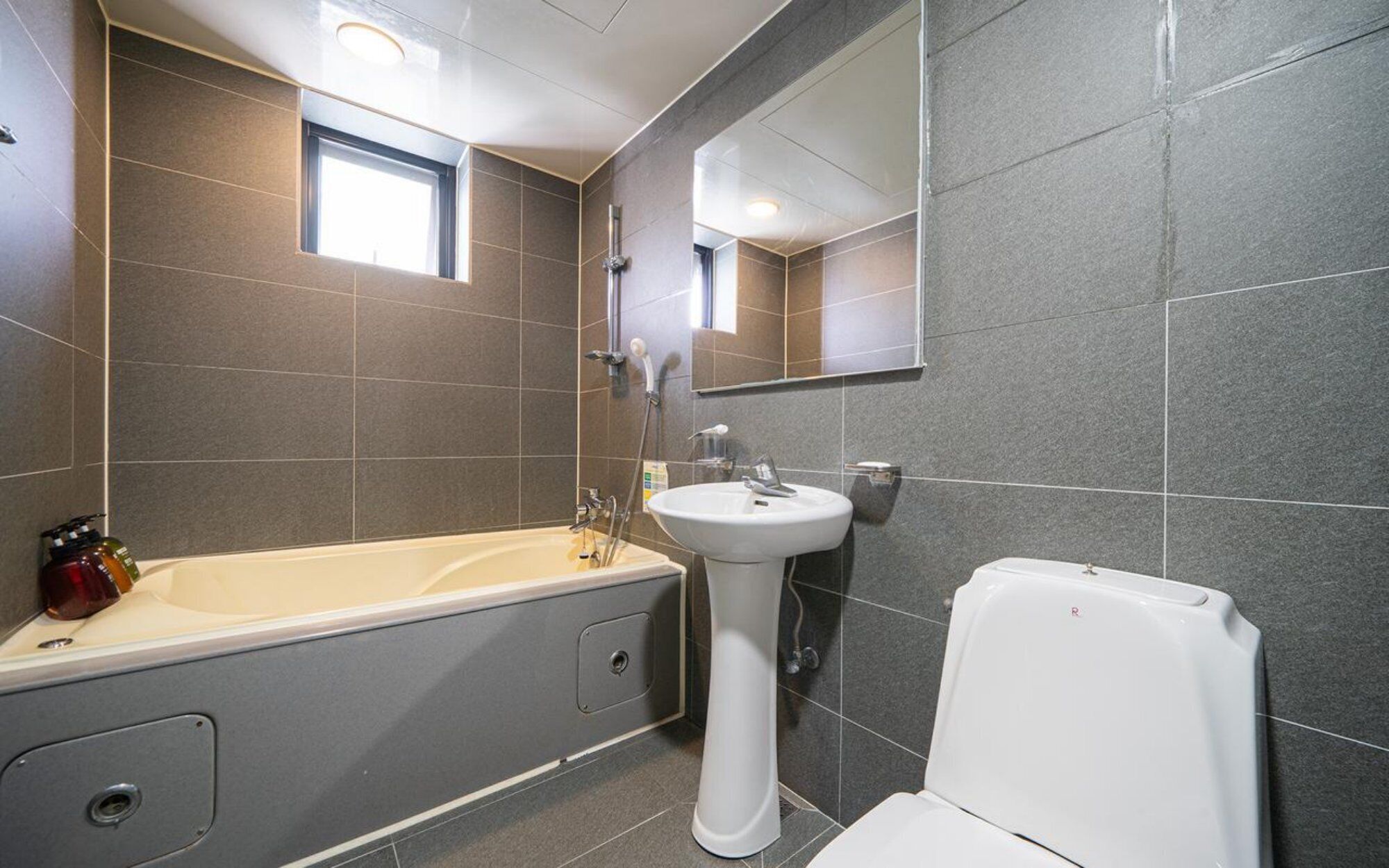 Un baño moderno con bañera, lavamanos pedestal, inodoro y espejo.