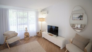 En moderne stue med et fladskærms-tv, to lænestole, et hvidt konsolbord, en gulvlampe og et stort spejl på væggen.