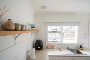 Eine Küche mit Kaffeemaschine, Wasserkocher, Spüle und einem Fenster mit Jalousien.