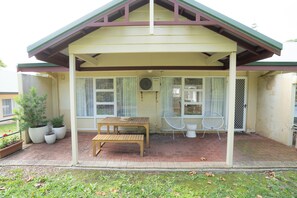 A covered patio with a table and chairs, potted plants, and a window with curtains. - Self contained villa, Middleton Rd Cottage (Mira Mar)