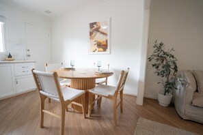 Ein Essbereich mit einem runden Tisch, vier Stühlen, einem Blumentopf und einer weißen Wand mit einem gerahmten Bild.