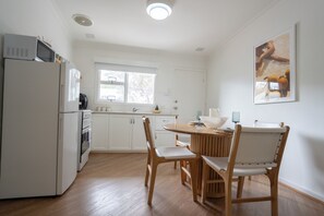 A kitchen with white cabinets, a refrigerator, an oven, a dining table with chairs, and a window. - Self contained villa, Middleton Rd Cottage (Mira Mar)