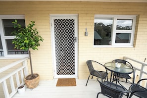 Eine Veranda mit einem Blumentopf, einer Tür mit einem Schutzgitter, einem Tisch mit Stühlen und einem Fenster.