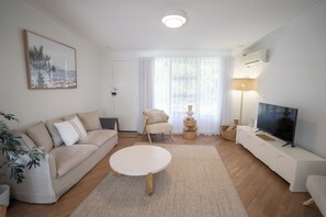 A living room with a sofa, a round coffee table, a TV, and a lamp. - Self contained villa, Middleton Rd Cottage (Mira Mar)