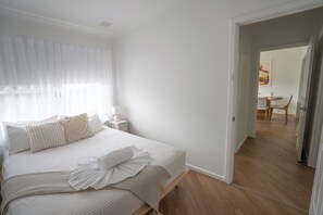 A bedroom with a bed, bedside table, and a view into another room. - Self contained villa, Middleton Rd Cottage (Mira Mar)