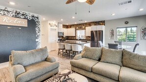 Ein Wohnzimmer mit einer Couch und Hocker, einem Deckenventilator und einer Küche im Hintergrund.