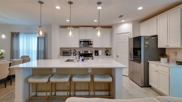 Una cocina moderna con una isla central, taburetes de bar, electrodomésticos de acero inoxidable e iluminación colgante.
