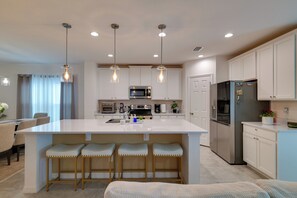 Una cucina moderna con isola centrale, sgabelli da bar, elettrodomestici in acciaio inossidabile e illuminazione a sospensione.