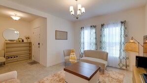Una sala de estar con sofá, mesa de centro, mueble para televisor, lámpara y candelabro.