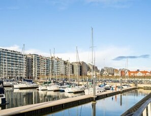 Ein Yachthafen mit vertäuten Booten, eine Uferpromenade und mehrstöckige Gebäude im Hintergrund.