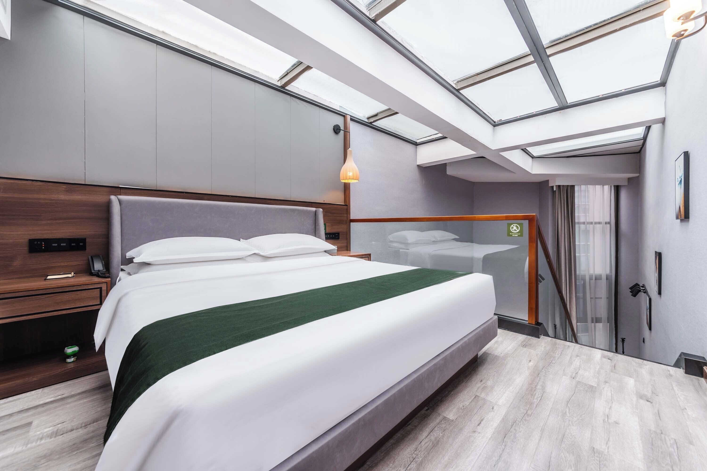 A modern hotel room with a large bed, a wooden nightstand, a desk, and a skylight.