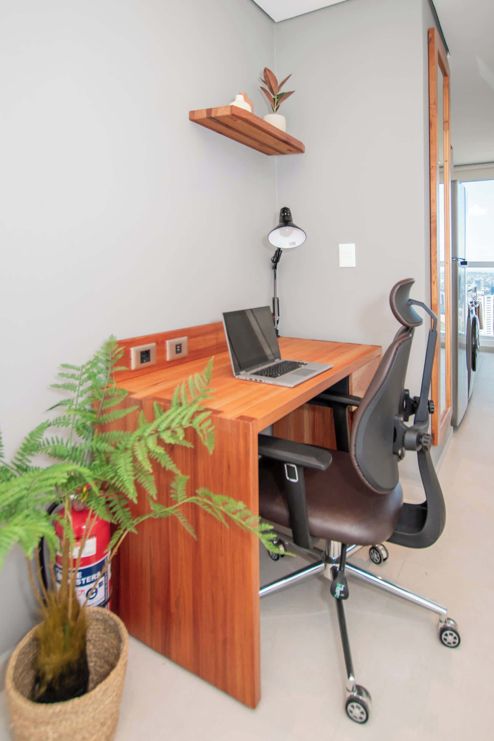 Un escritorio de madera con una computadora portátil, una silla, una planta en maceta y un extintor.
