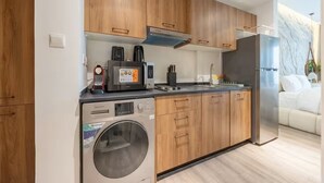 A modern kitchen with wooden cabinets, a built-in washing machine, a refrigerator, and a coffee maker. - Bloomfields Studio - Oasis 1 - Masdar (Abu Dhabi)