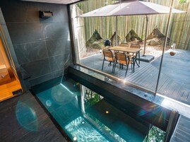Piscina interior moderna con pared de vidrio, cubierta de madera y asientos exteriores.