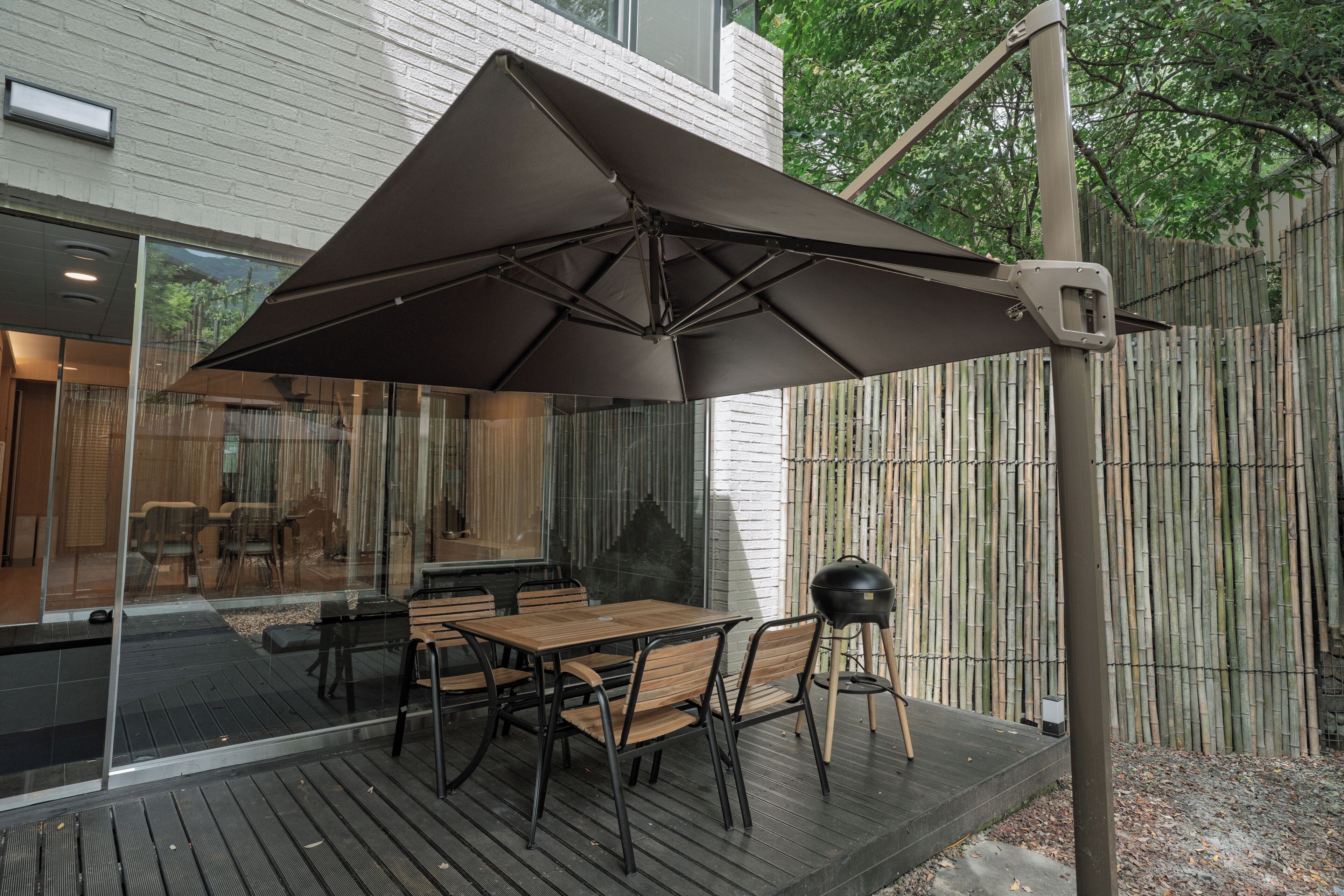 An outdoor patio with a table and chairs, a large umbrella, and a grill.
