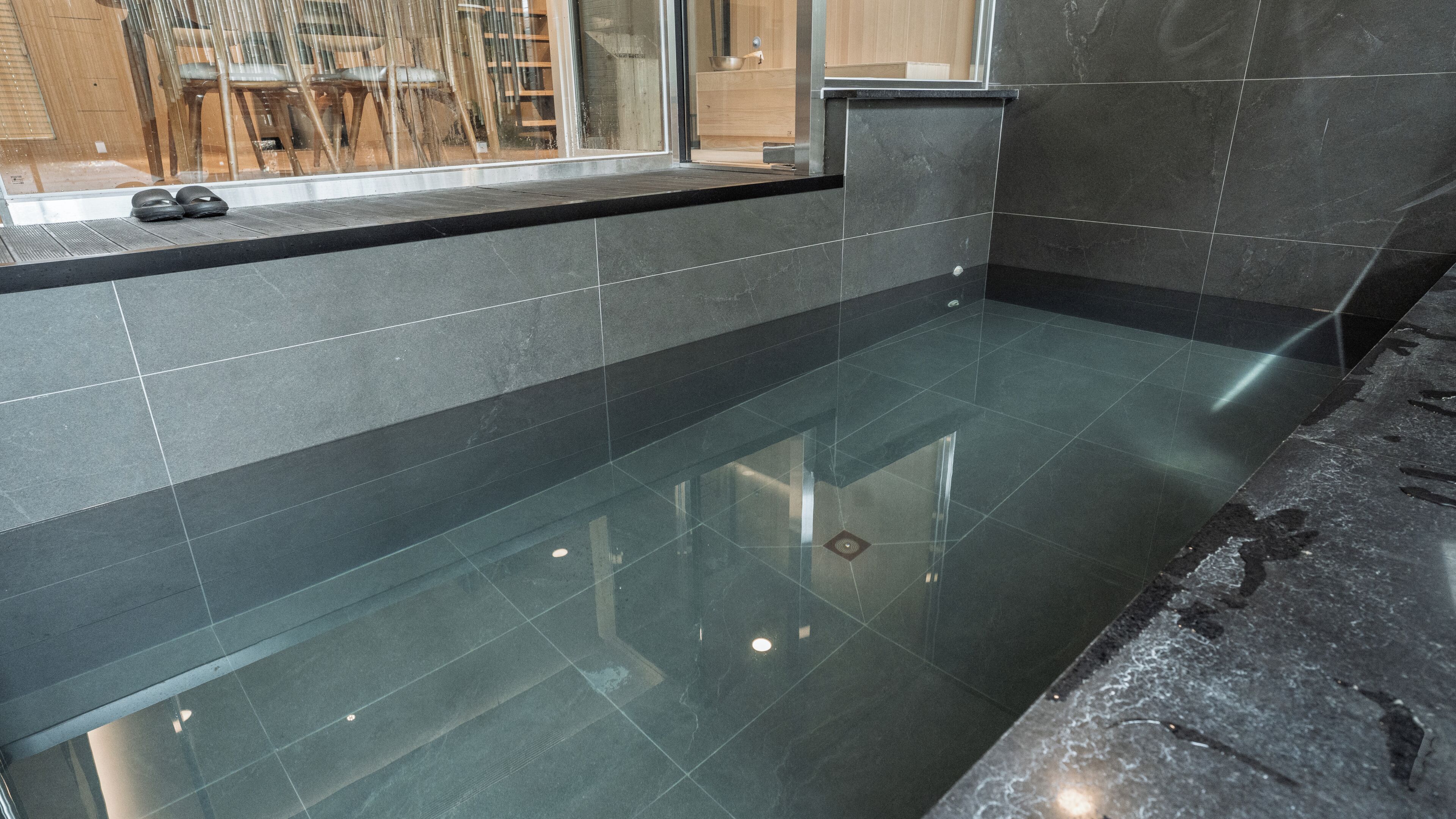 Une salle de bain moderne avec une douche à l’italienne délimitée par des parois de verre, un plan de toilette noir et un sol carrelé.