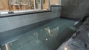 Une salle de bain moderne avec une douche à l’italienne délimitée par des parois de verre, un plan de toilette noir et un sol carrelé.